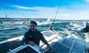 Boris Herrmann in Kiel, auf seinem Boot mit Solarpaneelen, umgeben von anderen Booten und Segelschiffen auf dem Meer.