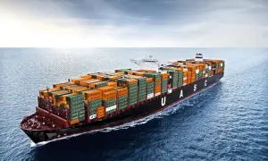 Ein riesiges Containerschiff mit orangefarbenen und grünen Frachtcontainern fährt auf dem Meer. Die UASC-Schriftzüge sind gut sichtbar. Die globale Logistik ist auf dem Weg, die Transitzeit zu optimieren.