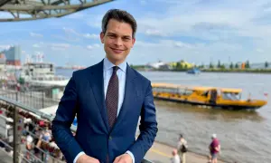 Ein Mann im Anzug steht am Hafen. Im Hintergrund fährt ein gelbes Ausflugsboot. Er ist ein port agent, der die Schiffe im Blick hat.