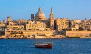 Ein Boot fährt im malta port vor der Skyline von Valletta mit der Kuppel der St. Paul's Cathedral.