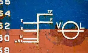 Schiffsbord mit Markierungen, die die Tiefgangslinien (plimsoll line) anzeigen. Zahlen und Buchstaben wie 56, 54, 52, 50, 68, T, S, W, WNA, TF, F, V, O, L sind sichtbar.