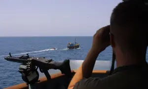 Mann mit Fernglas beobachtet ein Schiff, während ein Maschinengewehr bereitsteht. Möglicherweise ein Einsatz von Smit Salvage.