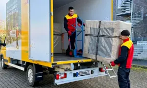 Zwei Männer laden ein großes Paket aus einem LKW. Ein Mann schiebt es mit einem Hubwagen, der andere trägt es. Maersk e-delivery macht es möglich.