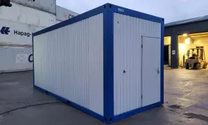 Ein blauer und weißer Container steht auf einem Container-Depot. Im Hintergrund sind weitere Container und ein Gabelstapler zu sehen.