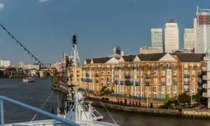 Blick auf den London Harbour mit modernen Hochhäusern und einem Flussufer mit Backsteinbauten. Ein Schiff liegt im Vordergrund.