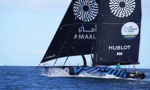 Segelboot mit schwarzen Segeln und blauen Wellenmuster auf dem Rumpf, das auf dem Meer fährt.