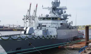 Graue corvette F266 im Hafen, mit Kranen und Containern im Hintergrund.