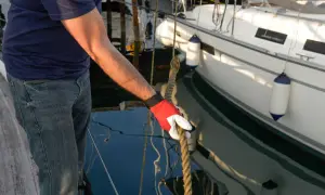 Mann mit roter Handschuh hält Seil an einem vertäuten Schiff.