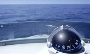 Kompass auf einem Boot zeigt die Richtung auf dem Meer. Teile des Bootes wie das Deck und die Windschutzscheibe sind sichtbar.