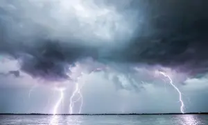 Ein heftiges Gewitter erhellt den Himmel über dem Meer. Blitze zucken, während ein einsames Segelboot auf dem Wasser treibt.