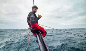 Boris Herrmann winkt lässig vom Bug seines Bootes, umgeben von rauer See und Segeltrossen.