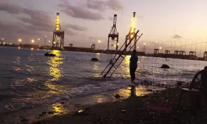 Abendstimmung am Hafen von Port Sudan. Kräne leuchten im Wasser, eine Person steht am Ufer.