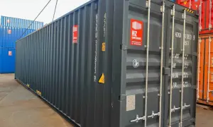 Ein grauer soc container wird von einer Kette angehoben. Daneben stehen blaue und rote Container.
