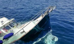 Ein sinkendes Boot neigt sich gefährlich im tiefblauen Meer. Rettungsringe und Fender treiben im Wasser.