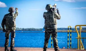 Zwei Soldaten sichern die Küste. Einer richtet eine Waffe, der andere hält ein Gerät. Maritime security in Aktion.