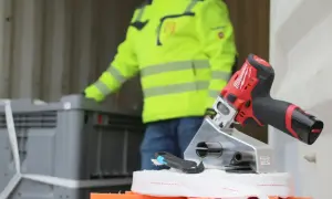 Werkzeug für Container Lashing: Ein Mann in Warnweste lädt Kisten, während ein Akkuschrauber und ein Cutter bereitliegen.