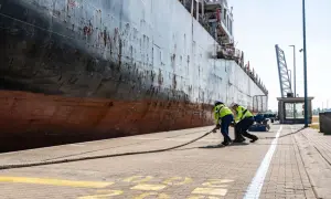 Zwei Hafenarbeiter ziehen ein dickes Seil am Antwerpen Port. Ein riesiges Schiff liegt am Kai.