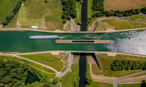 Ein großes Frachtschiff fährt auf einem Kanal. Daneben liegt eine Schleuse, bereit für das nächste Schiff.