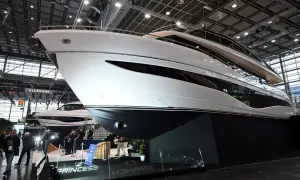 Eine glänzende weiße Luxus-**Boot**-Yacht mit dunklen Fenstern, ausgestellt auf einer Messe. Im Hintergrund eine weitere Yacht und Besucher.