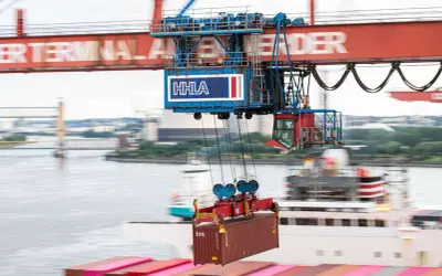 Ein großer Kran hebt einen Container im Mumbai Port. Die HHLA-Beschriftung ist auf dem Kran zu sehen.