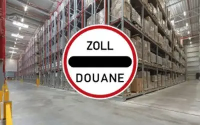 Großes Lager mit hohen Regalen voller Waren. Ein Schild mit "ZOLL DOUANE" weist auf einen bonded store hin.