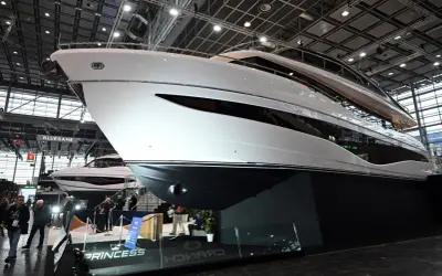 Eine glänzende weiße Luxus-**Boot**-Yacht mit dunklen Fenstern, ausgestellt auf einer Messe. Im Hintergrund eine weitere Yacht und Besucher.