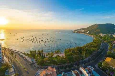 Sonnenuntergang über dem Vung Tau Port mit vielen Booten im Wasser und einer grünen Hügelkette im Hintergrund.