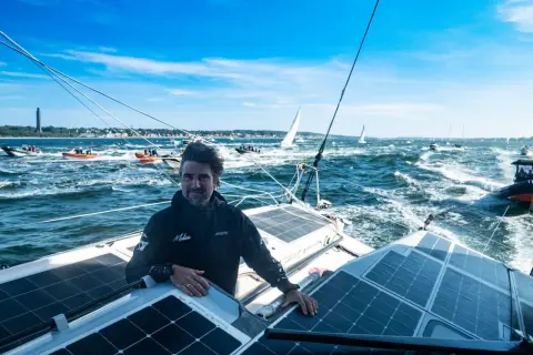 Boris Herrmann in Kiel, auf seinem Boot mit Solarpaneelen, umgeben von anderen Booten und Segelschiffen auf dem Meer.