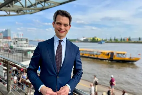 Ein Mann im Anzug steht am Hafen. Im Hintergrund fährt ein gelbes Ausflugsboot. Er ist ein port agent, der die Schiffe im Blick hat.