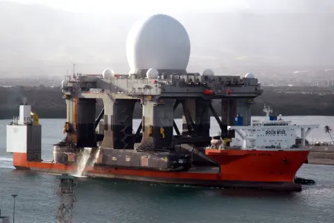 Die orangefarbene "Blue Marlin" ist ein Schwergutfrachter, der eine riesige Plattform mit einer großen weißen Kuppel transportiert.