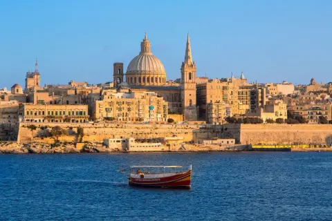 Ein Boot fährt im malta port vor der Skyline von Valletta mit der Kuppel der St. Paul's Cathedral.
