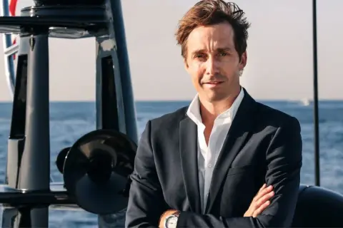 Martin Hager, mit verschränkten Armen auf einem Boot, blickt zuversichtlich in die Kamera.