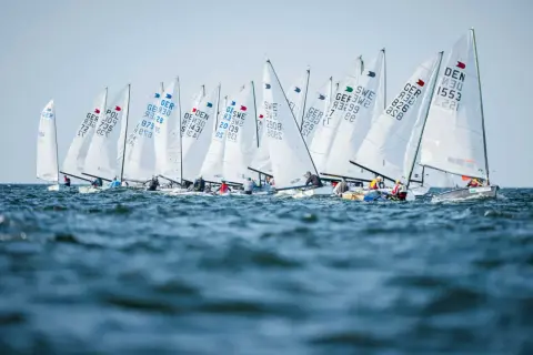 Viele Boote segeln bei der Kieler Woche. Die weißen Segel sind mit Länderkürzeln und Nummern beschriftet.
