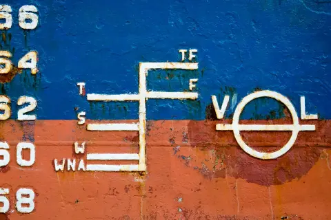 Schiffsbord mit Markierungen, die die Tiefgangslinien (plimsoll line) anzeigen. Zahlen und Buchstaben wie 56, 54, 52, 50, 68, T, S, W, WNA, TF, F, V, O, L sind sichtbar.