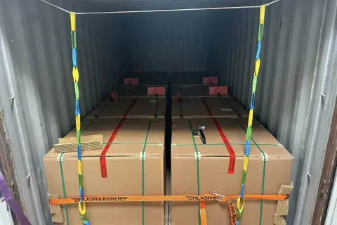Ladungssicherung in einem Frachtcontainer: Mehrere große Kartons, gesichert mit Gurten und Ketten. Verschiedene Arten von Containern werden hier für den Transport genutzt.