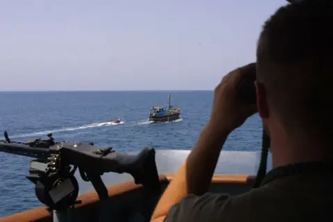 Mann mit Fernglas beobachtet ein Schiff, während ein Maschinengewehr bereitsteht. Möglicherweise ein Einsatz von Smit Salvage.