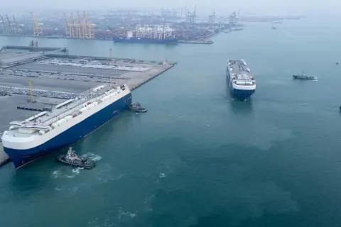 Große Autotransporter im Hafen, bereit für den Roll-on/Roll-off-Verkehr. Schlepper assistieren beim Manövrieren.