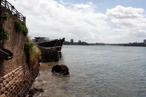 Ein Schiff liegt im Hafen von Mombasa vor Anker. Die Steinküste und Gebäude im Hintergrund zeugen von der geschäftigen Atmosphäre.