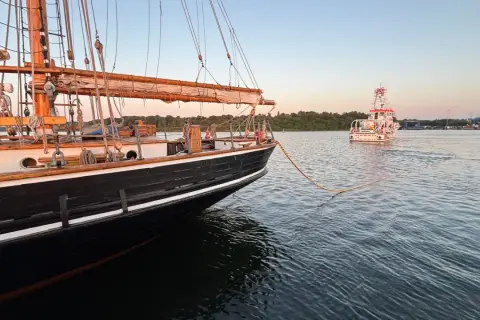 Ein majestätisches Albatros Segelschiff wird von einem Schlepper gezogen. Die Sonne geht unter und taucht das Wasser in ein warmes Licht.