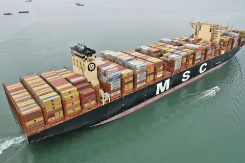 Die MSC Irina, ein riesiges Containerschiff, transportiert Fracht über das Meer. Ein kleines Beiboot fährt nebenher.