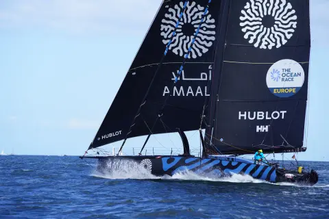 Segelboot mit schwarzen Segeln und blauen Wellenmuster auf dem Rumpf, das auf dem Meer fährt.