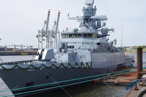 Graue corvette F266 im Hafen, mit Kranen und Containern im Hintergrund.