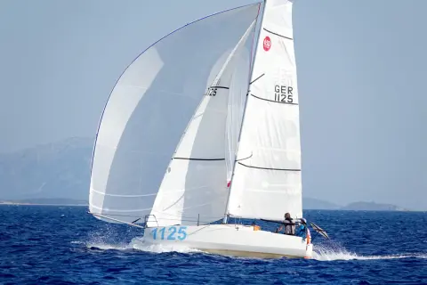 Segelboot mit zwei Personen an Bord, das auf dem Meer fährt. Die Segel sind weiß und mit der Nummer 1125 beschriftet. Dies ist ein Bild von einem Mini Transat Rennen.