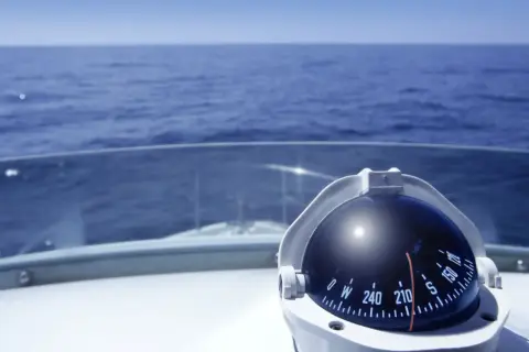 Kompass auf einem Boot zeigt die Richtung auf dem Meer. Teile des Bootes wie das Deck und die Windschutzscheibe sind sichtbar.