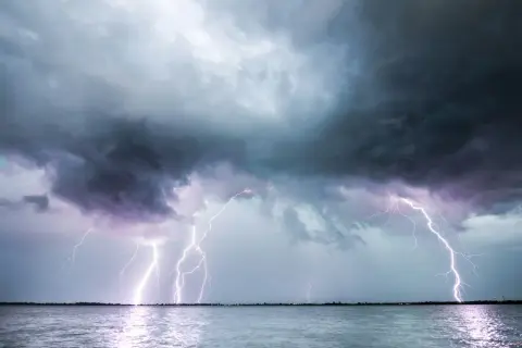 Ein heftiges Gewitter erhellt den Himmel über dem Meer. Blitze zucken, während ein einsames Segelboot auf dem Wasser treibt.