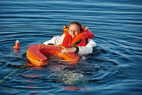 Frau im Wasser mit Schwimmweste und Rettungsring, ein "man overboard" Szenario.