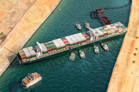 Ein Containerschiff wird von mehreren Schleppern durch einen Kanal manövriert. Der allgemeine Durchschnitt der Frachtschifffahrt.