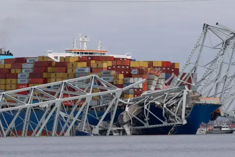 Ein Frachtschiff kollidiert mit einer Brücke, die in sich zusammenfällt. Container sind gestapelt, ein Zeichen für die globale Logistik, die in den US Ports stattfindet.