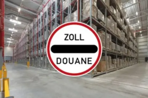 Großes Lager mit hohen Regalen voller Waren. Ein Schild mit "ZOLL DOUANE" weist auf einen bonded store hin.