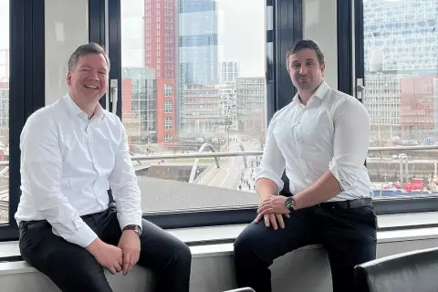 Zwei Männer, ein maritimer Anwalt und sein Kollege, sitzen vor einem Fenster mit Blick auf die Hamburger Hafencity.